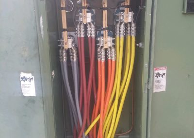 Electrical utility box with six large colored cables—gray, red, orange, yellow—connected to metal terminals, door open, safety warning labels visible.