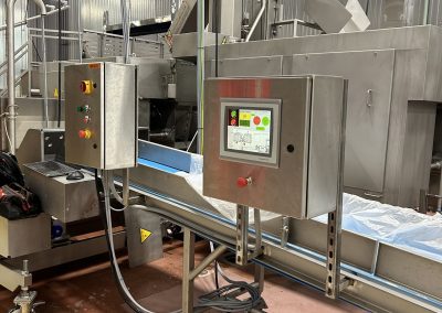 Industrial food processing machine with control panels, conveyor belt, and stainless steel surfaces in a factory setting.