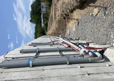Electrical conduit pipes run along a concrete wall at a construction site, with caution tape and gravel visible on the ground.