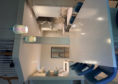 Modern kitchen with a large marble island, blue chairs, mosaic tile backsplash, stainless steel appliances, pendant lights, and white cabinetry.